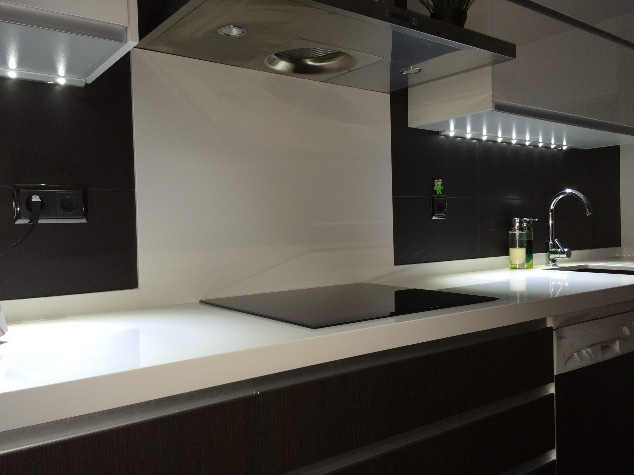 Cocina con encimera blanca y pared revestida en tonos oscuros